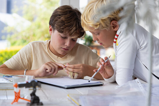 pre teen and early teen boy doing homework together in light filled room