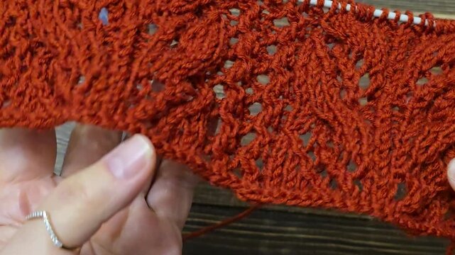 The process of knitting a multicolored openwork yoke for a jumper or cardigan. The raised pattern is on circular needles, and the work is placed on a dark wooden table.