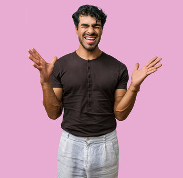 Young hispanic man, casual winner excited by success, celebrating mad win with arms raised in a crazy studio portrait, screaming with joy