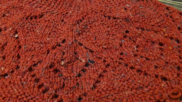 The process of knitting a multicolored openwork yoke for a jumper or cardigan. The raised pattern is on circular needles, and the work is placed on a dark wooden table.