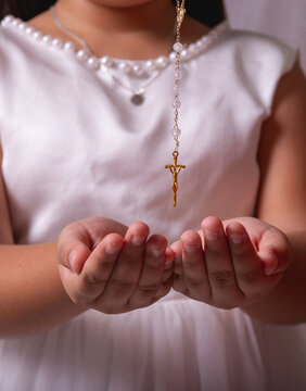 Young Girl in White Dress Holding Hands Beneath a Gold Rosary