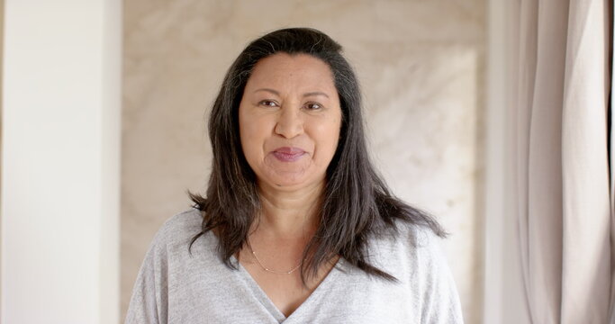 Woman standing poised in residential interior wearing light grey V-neck top and thin gold necklace
