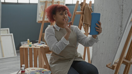 Woman with red hair holds tablet and paintbrush, brush to lips in studio  concentration creativity inspiration. © Krakenimages.com