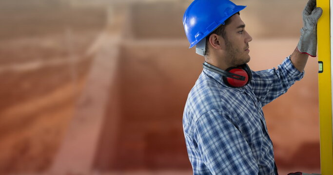 Construction worker in blue hard hat using level tool at building site