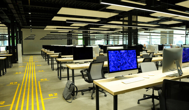 Modern high tech company open plan office workspace with turned on computer monitors on wooden desks without people