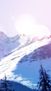 Vertical video: Sun shifting over snow ridge, lens flare growing and washing slope to accent crest