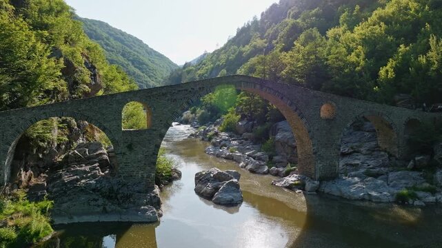 Devils Bridge ancient Ottoman stone arch bridge over Arda River in Rhodope Mountains forest aerial drone shot historical landmark tourism in Bulgaria stock footage