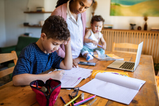 Mother helping son with homework as baby sits nearby