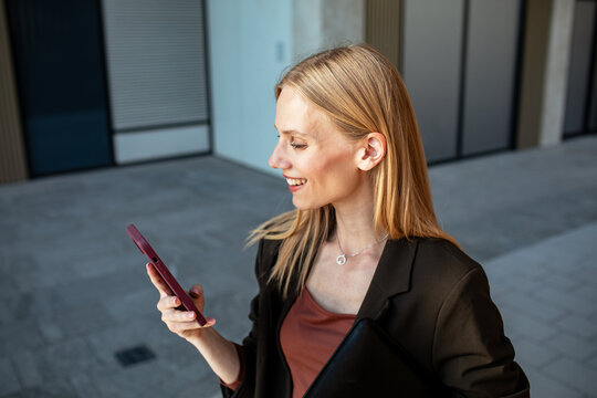 Smiling businesswoman checking smartphone outside office