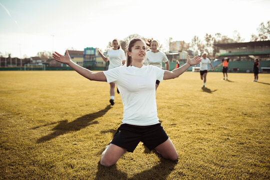 Female soccer player kneels to celebrate goal on field