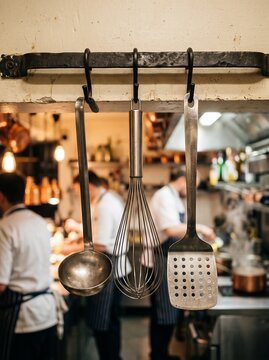 Professional Kitchen Utensils Hanging on Rack with Chefs Working in Background