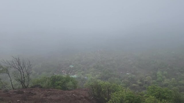 Aerial drone footage smoothly descends through thick mountain mist to reveal a lush green valley forest, capturing a cinematic atmosphere perfect for nature and travel projects.