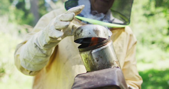 Caucasian male beekeeper in protective clothing preparing smoker