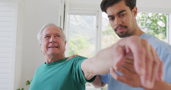Male physiotherapist rotating retired senior man's hand in clockwise motion at retirement home