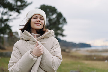 Young woman in a warm puffer coat and knit beanie enjoying a chilly day outdoors by a windswept field, smiling and relaxed. © SHOTPRIME STUDIO