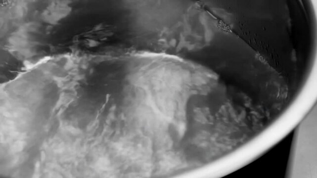 Boiling water bubbles and swirls inside a round pot in a tight closeup