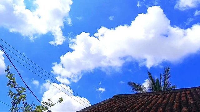 Sunny day with white clouds drifting across a clear blue sky above a house roof cloud rooftop weather cumulus daytime