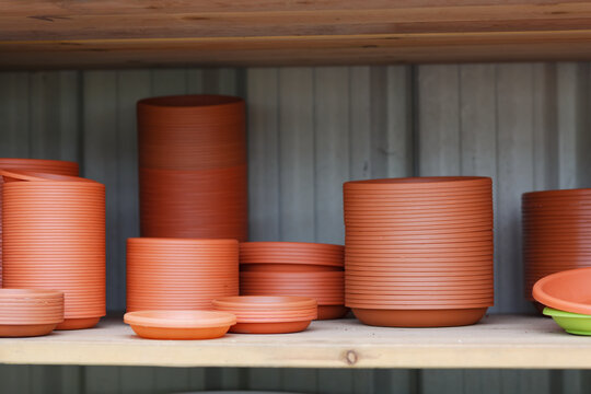 Stacked terracotta plastic plant pots and saucers on wooden shelves. Ribbed cylindrical containers of different sizes arranged in neat piles against a wooden wall. Gardening tools and flower pots