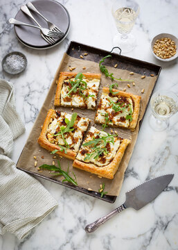 Tart with caramelized onions, cheese, and arugula on marble surface
