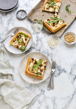 Caramelised onion and cheese tarts on marble surface with wine glasses