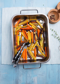 Colorful roasted carrots in baking dish with thyme and pepper mill