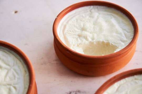 Three unglazed terracotta clay cups hold smooth strained yogurt