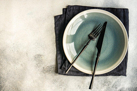 Ceramic plate with fork and knife on dark napkin overhead view