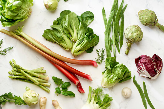 Vegan flat lay of fresh spring vegetables and greens on marble surface