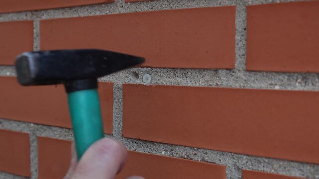 Hand using a hammer to drive a plastic wall plug into the mortar joint between red bricks