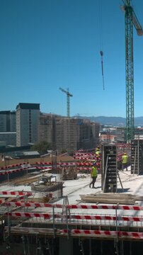 Construction site workers assemble column formwork around rebar using a tower crane on a building upper floor, captured in timelapse overlooking the sea