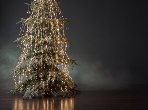Christmas tree with glowing fairy lights and ornaments on dark wooden floor