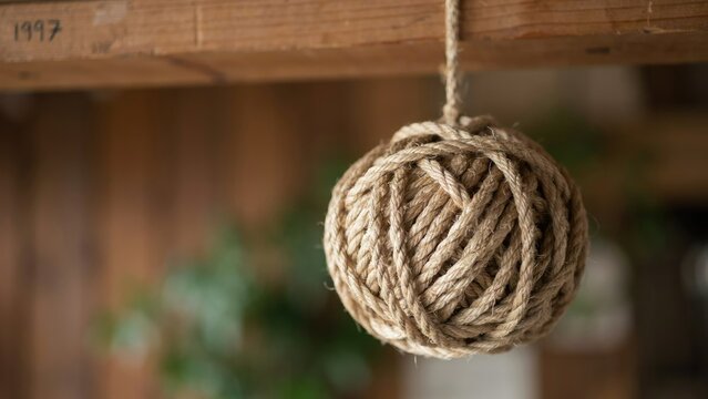 A close-up of a spherical ball of natural jute twine hanging from a wooden beam