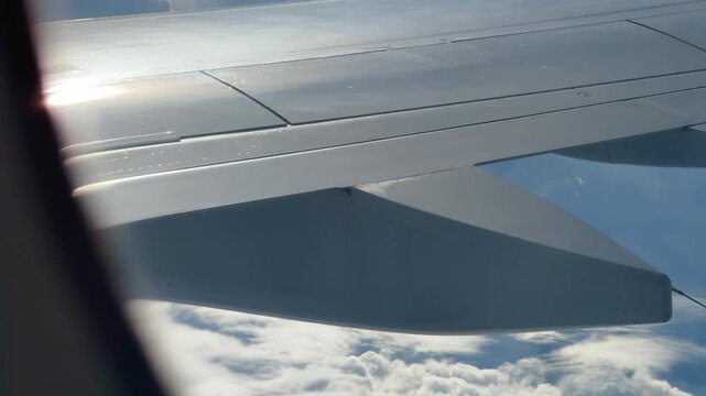 Airplane wing close up with sun glare through window above clouds during flight