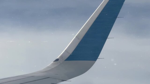 Close up of airplane wing tip winglet against gray cloudy sky in flight during the rain