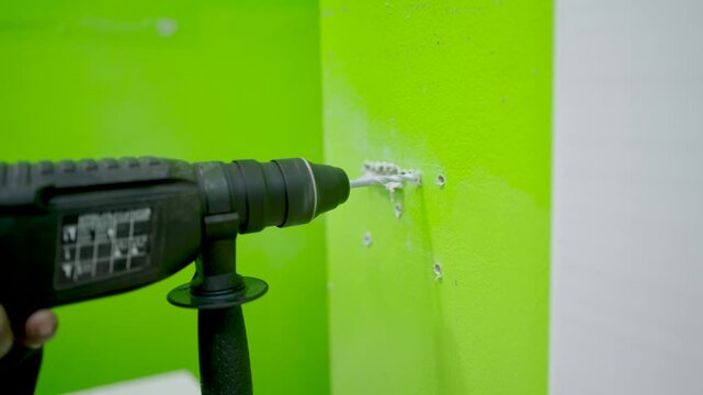 Worker uses electric drill for drilling or breaking into concrete walls.