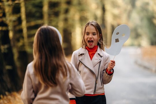 Two girls playing outdoors with a white paddle and surprised expression beside a forest path in soft natural light during an afternoon outing