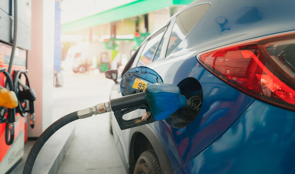 Blue car refueling with gasoline 95 at a petrol station during daytime, fuel nozzle filling vehicle tank for daily transportation, illustrating petroleum consumption, fuel cost and energy demand