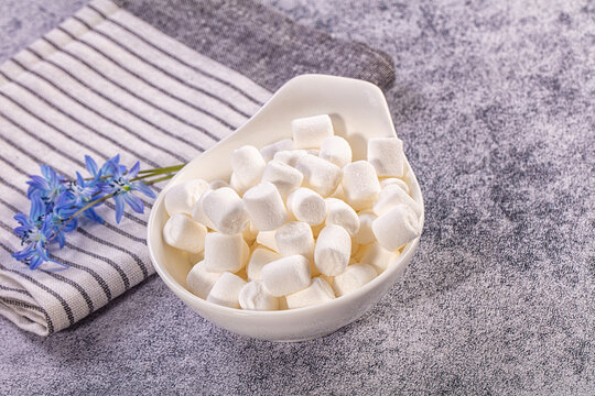 Striped linen napkin and blue hyacinth flowers beside white ceramic bowl filled with mini marshmallows dessert ingredient