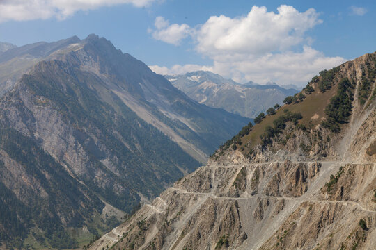 Winding mountain road carved into steep slopes of a deep valley under summer clouds, Ladakh, Kargil, India
