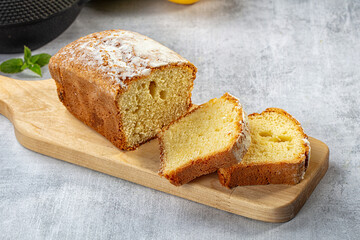 Wooden cutting board holding sliced golden pound cake dusted with powdered sugar, fresh mint leaf beside, on textured gray surface, dessert presentation © Andrei Starostin