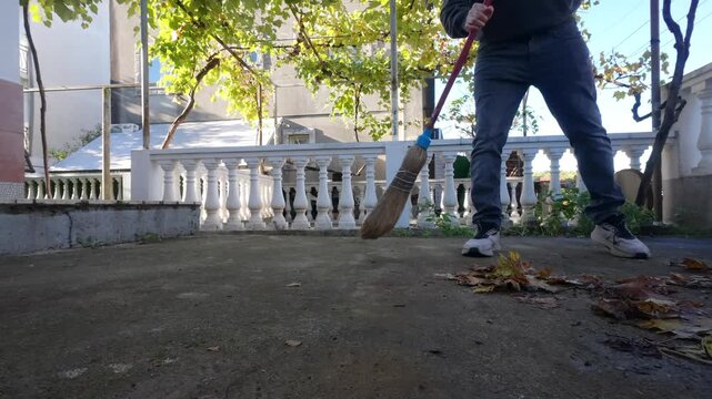 Low Angle Shot Of Sweeping Autumn Leaves With Broom