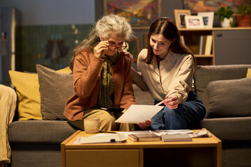 Young adult Caucasian woman helping senior Caucasian woman reviewing financial documents at home....
