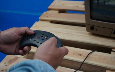 Hands holding a retro game controller while playing a video game on a classic monitor. Nostalgic gaming scene with selective focus, vintage technology and a softly blurred background. © Dr. CraftLab