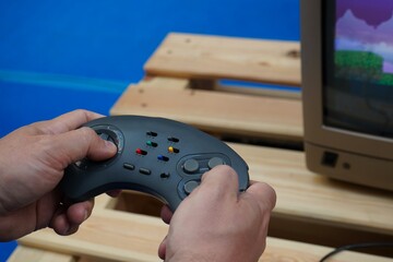 Hands holding a retro game controller while playing a video game on a classic monitor. Nostalgic gaming scene with selective focus, vintage technology and a softly blurred background. © Dr. CraftLab