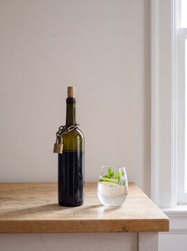 Wine bottle locked with a chain and padlock beside a glass of sparkling water
