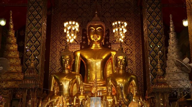 Interior view of the main hall in Wat Phra That Hariphunchai with golden Buddha statues and traditional Lanna decoration, Lamphun, Thailand.
