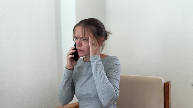During a work‑related phone call, a woman rubs her temple, experiencing a headache. Difficulties concentrating, stress, work load, lack of rest, and a decline in well‑being