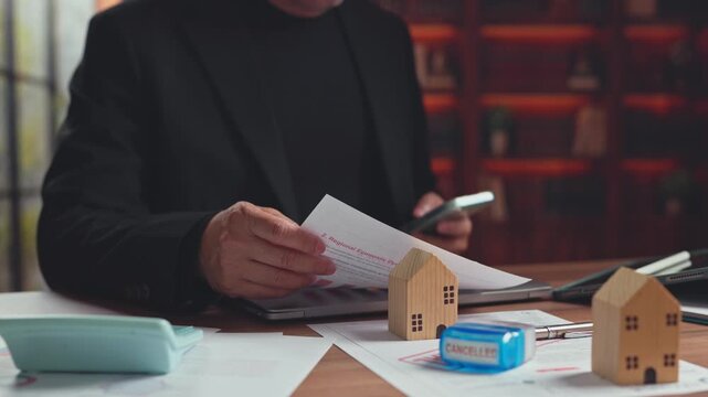 Investor reviews foreclosure document, cancellation stamp wooden house models at office desk. Mortgage default crisis, real estate loan cancellation, property investment financial risk analysis.