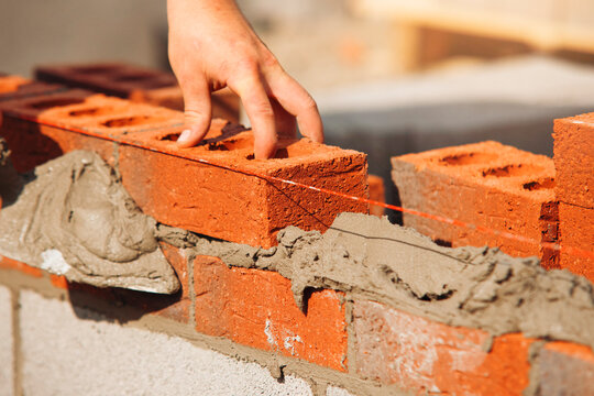 Worker laying red bricks along a mortar line at a construction site