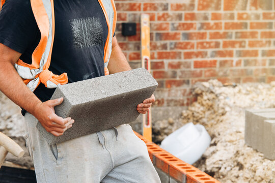 Construction worker carrying a concrete block beside a brick wall